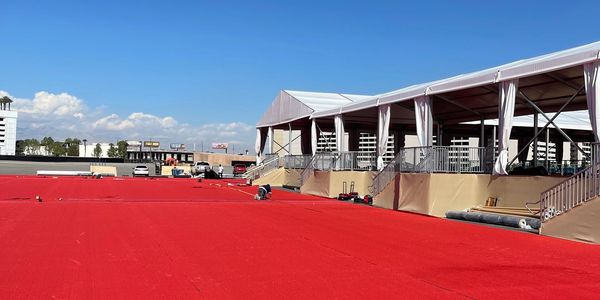 A large red carpet being laid out next to a white tent under a clear blue sky.