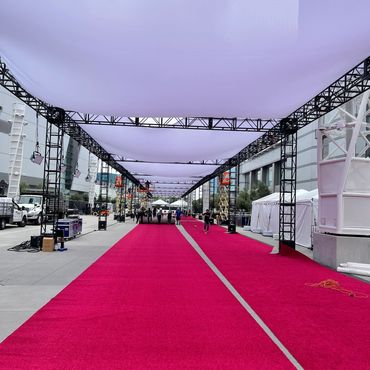 Workers preparing a red carpet event under white canopies.