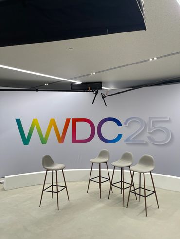 Empty chairs in front of a colorful WWDC25 backdrop in a studio.