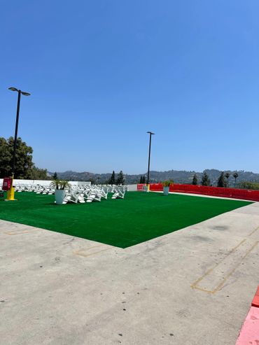 Outdoor seating area with white chairs on green artificial turf under a clear blue sky.