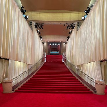 Grand red carpeted staircase with white drapes and spotlights.