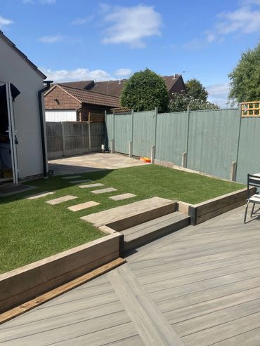 A neat backyard with green grass, stone stepping path, and wooden deck under a clear blue sky.