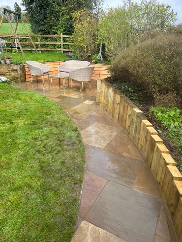 A cozy outdoor seating area on a wet stone patio beside a grassy lawn.
