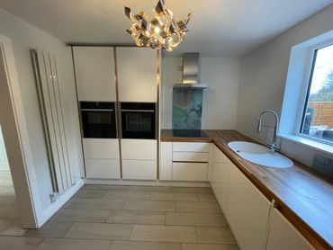 Modern white kitchen with wooden countertops and a unique chandelier.
