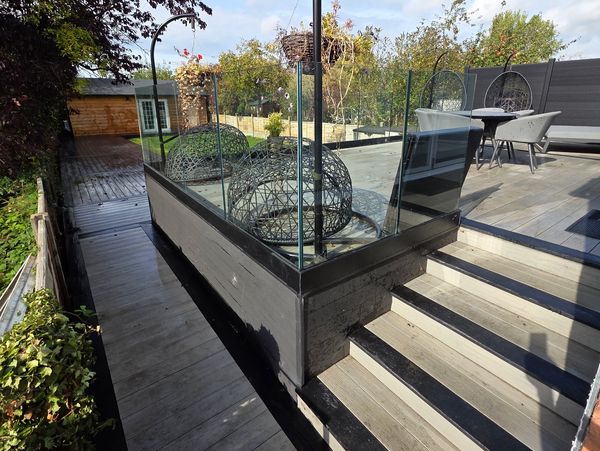 Modern outdoor patio with glass railings, hanging chairs, and a wooden deck under a clear sky.