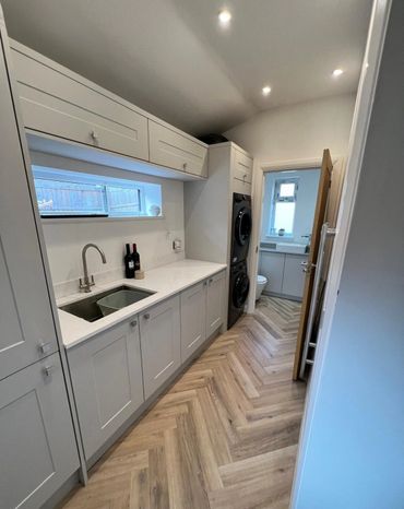 Modern laundry room with white cabinets and wood-patterned herringbone floor.