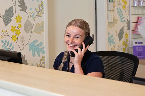 A photo of Jonathan Loughlin Dental's receptionist taking a phone call at reception with a big smile.