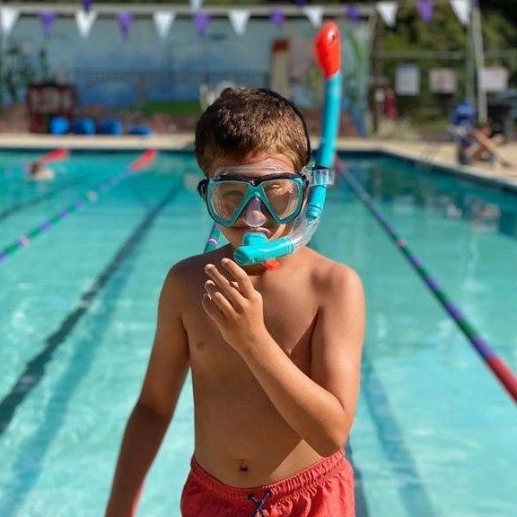 Kid by swimming pool wearing googles and snorkel