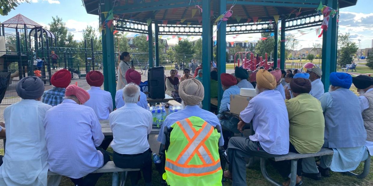 Group of people sitting in a park gazebo listening to a speaker.