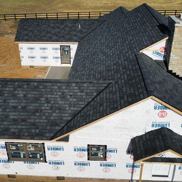 Partially constructed house with new black shingle roof.