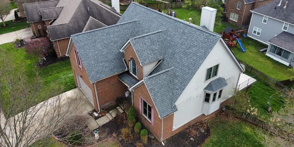 Aerial view of a suburban house with a gray roof and brick walls.