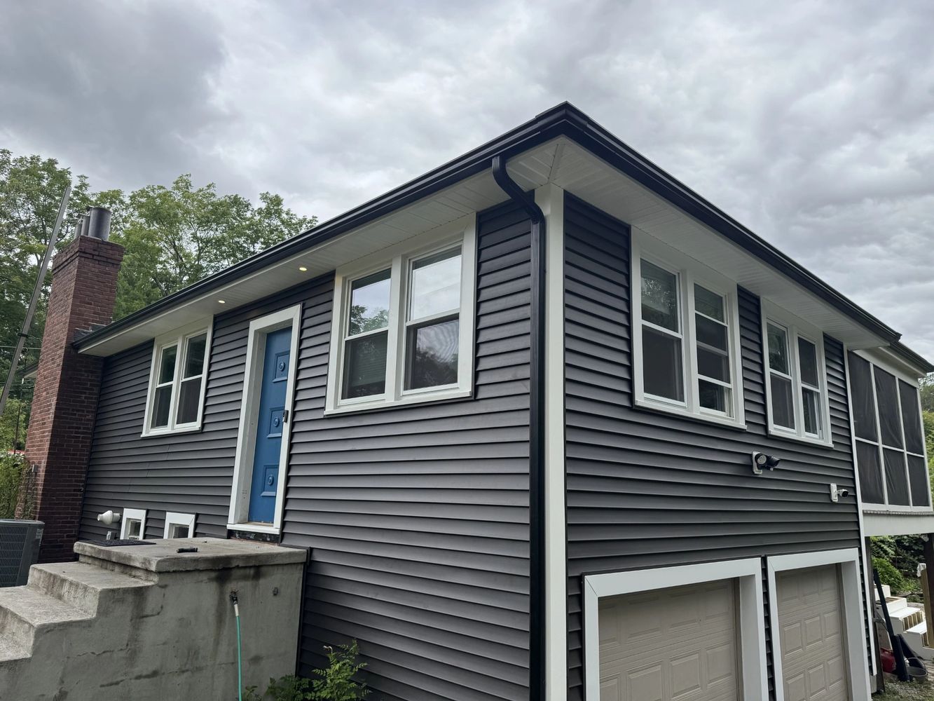 A modern house with gray siding and a blue door under a cloudy sky.