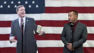 Man stands next to a cardboard cutout in front of an American flag.