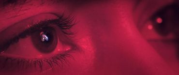Close-up of eyes with a galaxy reflected in the iris under red lighting.