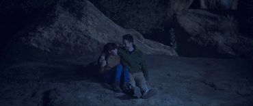 Couple sitting closely on a rock, sharing a warm moment at night.