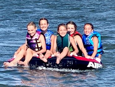 Five young girls with big smile riding a tube in Lake Pontchartrain near North Shore Beach.