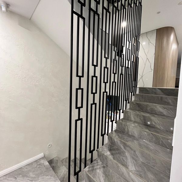 Modern staircase with gray marble steps and geometric black metal railing.