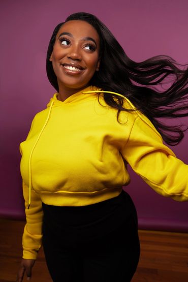 A woman wearing yellow swings her hair in motion while standing in front of a purple backdrop