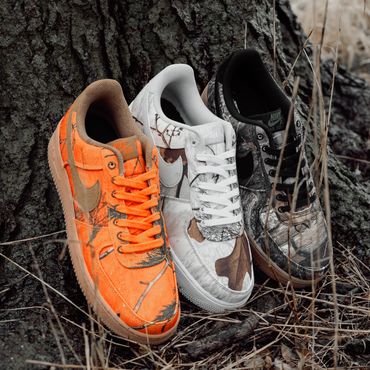 Three shoes of similar size and style stand against the base of a tree near tall dried grass