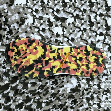 The patterned sole of a shoe lays visible in front of a background of a similar pattern