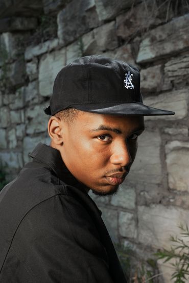 A closeup image of a man wearing a baseball hat with embroidered logo poses in front of a rock wall.