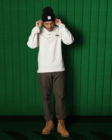 A man wearing a fall outfit and timberland boots stands in front of a green background
