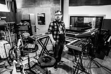 Brendan looking concerned while surrounded by guitars, synthesizers, and pianos