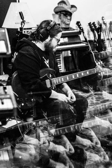 Caleb sitting with a guitar in the studio, listening to his new recordings.