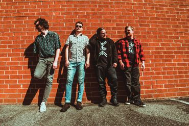 Generic band picture of Tiny City standing in front of a brick wall.