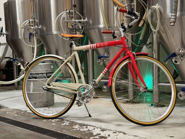 A red and cream bicycle parked in front of the brewery fermenters