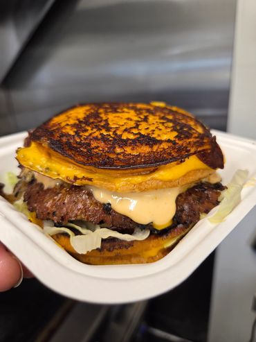 A close-up of a cheeseburger with melted cheese and sauce in a takeout container.