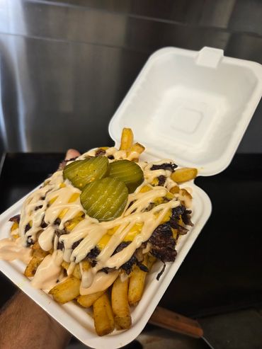 Loaded fries with cheese, sauce, and pickles in a takeout container.