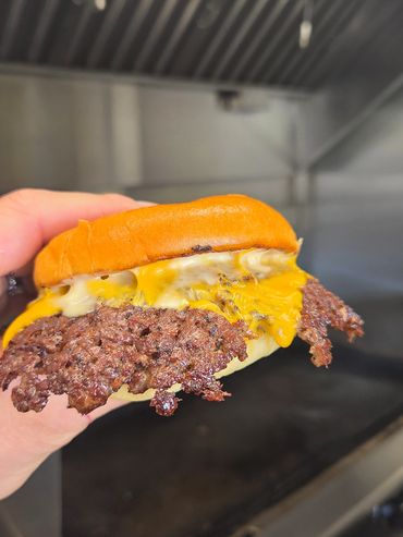 Hand holding a cheeseburger with crispy edges in a kitchen.