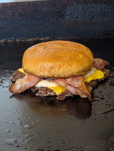 Bacon cheeseburger with melted cheese on a grill.