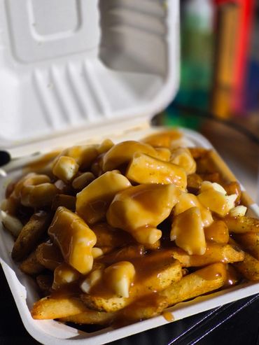 Close-up of poutine with fries, cheese curds, and gravy in a takeout container.