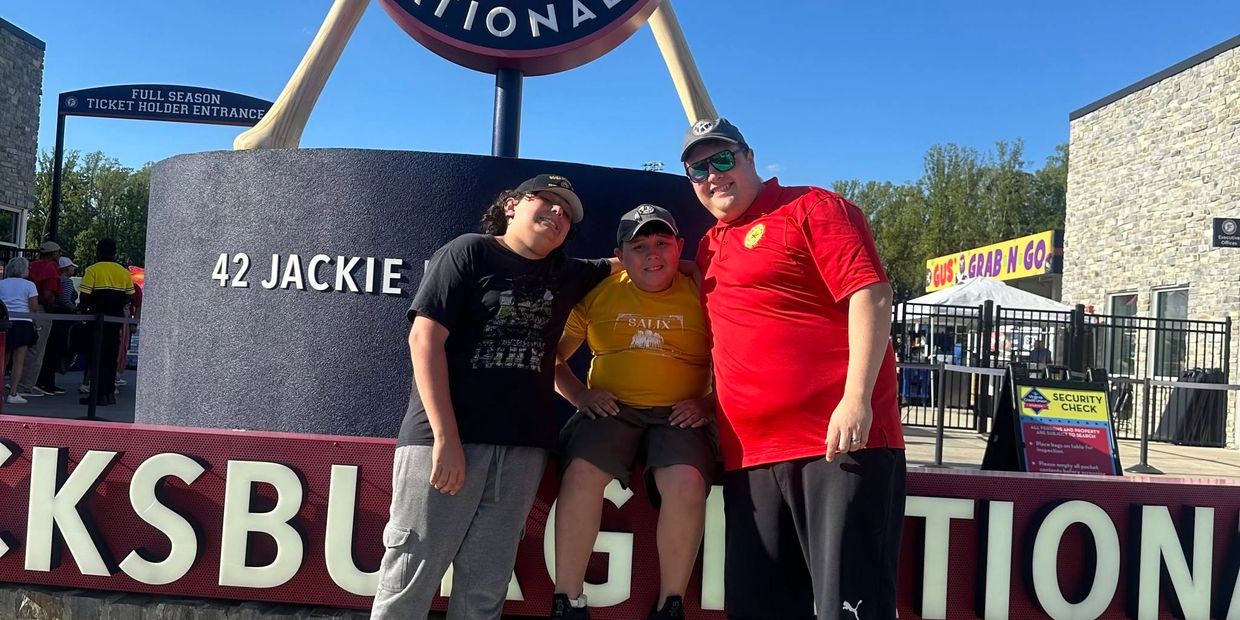 Three people posing in front of a stadium sign.