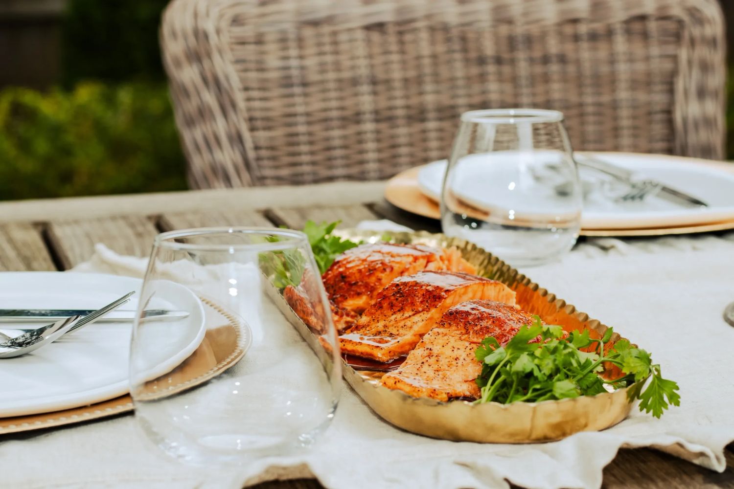 Grilled salmon fillets served with fresh herbs on a brass tray at an outdoor table.