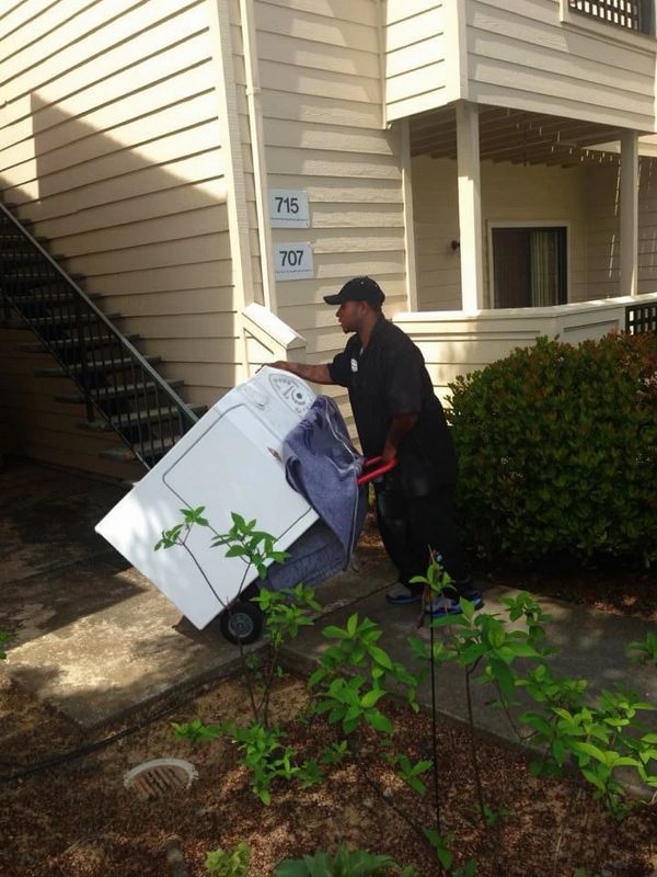 A man moving a washing machine on a dolly outside an apartment building.