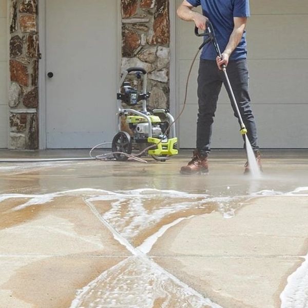 Person using a pressure washer to clean a driveway.