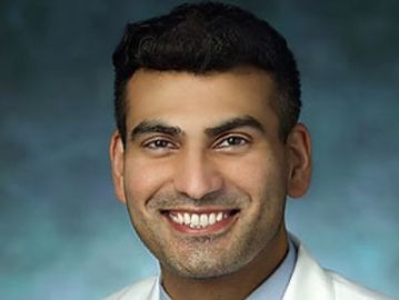 Smiling man in professional attire with a blue background.