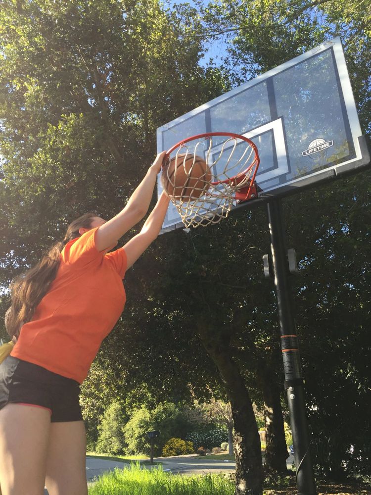 Young woman dunking a basketball outdoors on a sunny day.