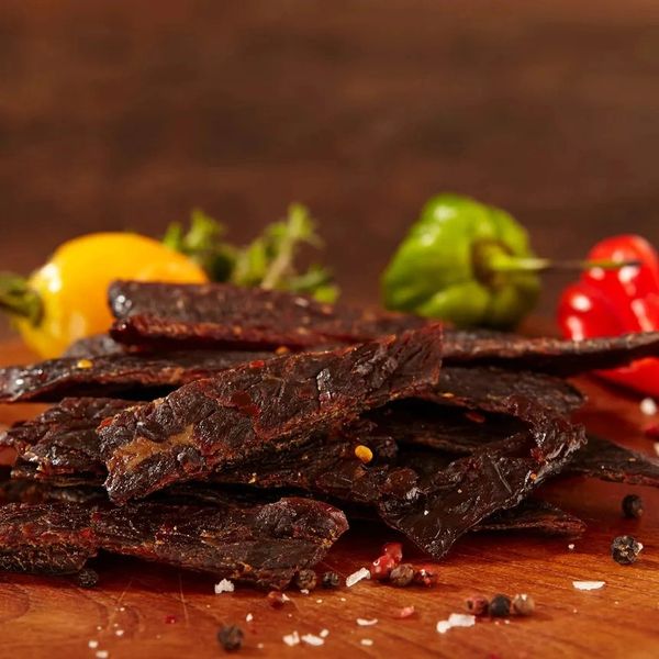 Close-up of spicy beef jerky with colorful peppers in the background.