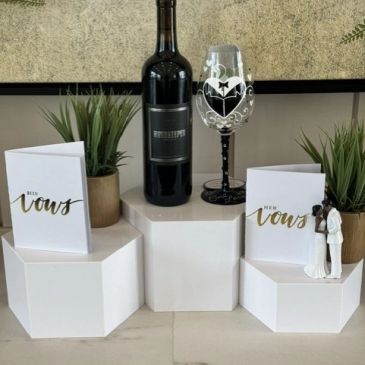 Wedding vow cards, wine bottle, decorated glass, and couple figurine.