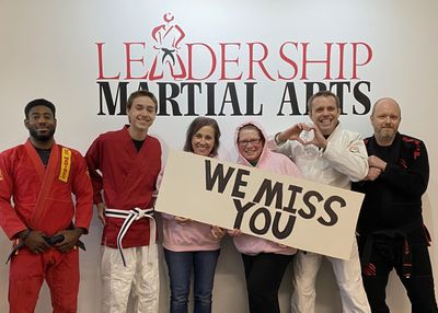 A group of martial artists holding a "We Miss You" sign.