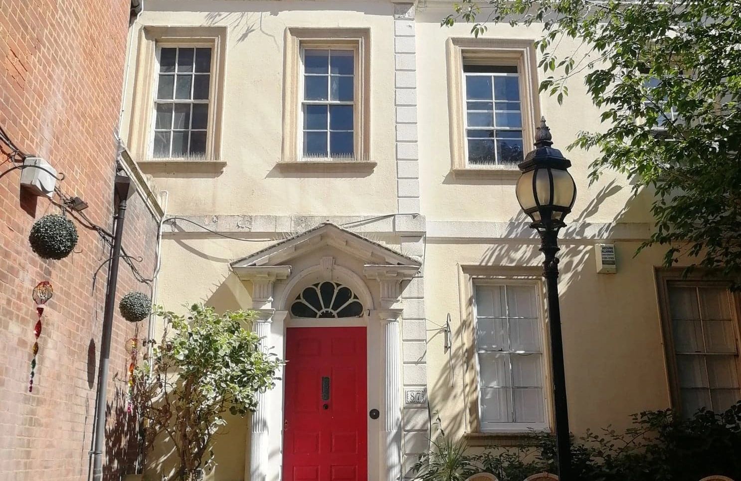 Beige terrace house with a grand red door and ornate lamppost outside