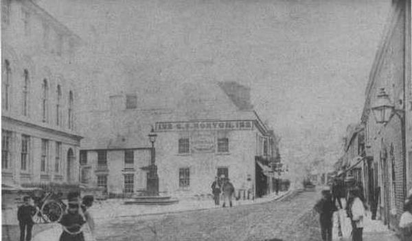 Old faded photo of the high street with figures and wagons outside a prominent white building