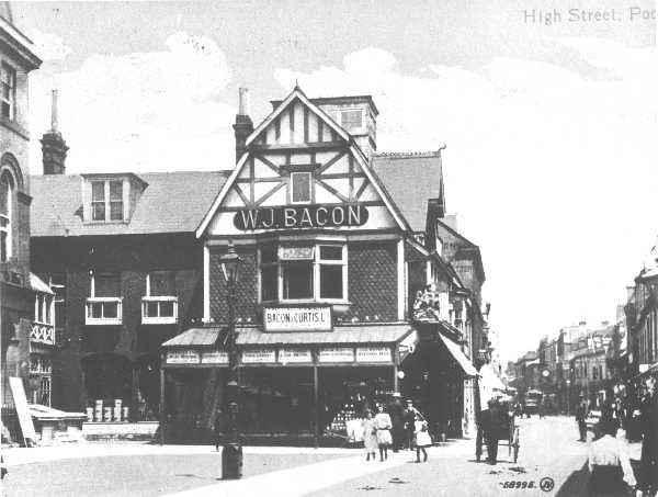 A photo of an old building with wooden beams & large sign reading 'W.J.Bacon' on a busy high street