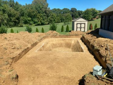 Excavated ground site for a future pool in a backyard on a sunny day.