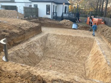 Workers prepare a large backyard excavation for a swimming pool installation.