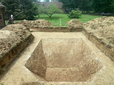 Excavated pool foundation with workers and surveying equipment nearby.